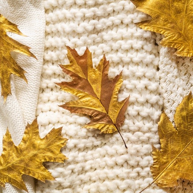 fall background with warm sweaters. pile of knitted clothes with autumn leaves, warm background, knitwear, space for text